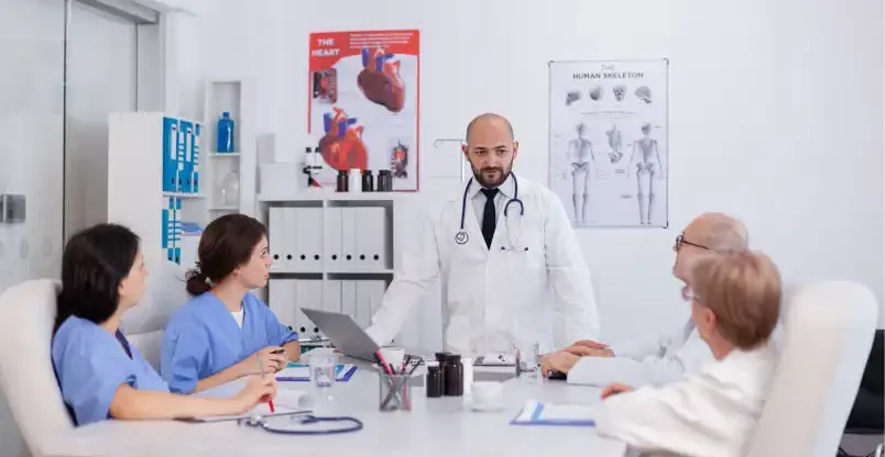 Cardiology-Claim-Processing-4-Proven-Strategies-to-Reduce-Denials-and-Boost-Revenue A doctor discusses medical topics with colleagues in a meeting room, emphasizing collaboration and teamwork.