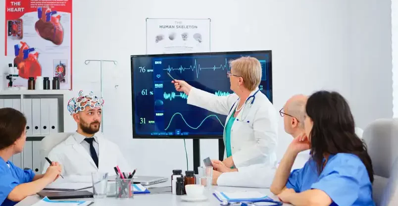 How-EHR-Has-Changed-Cardiology-Practice A group of doctors discussing in a meeting room, seated around a table with medical charts and laptops.